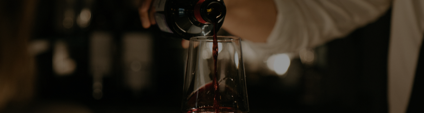 Man Pouring Red Wine in a Dark Bar